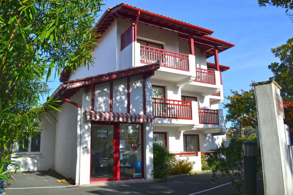 Façade de la résidence Izarenéa à Hendaye : bâtiment blanc aux balcons et encadrements rouges, dans le style basque.